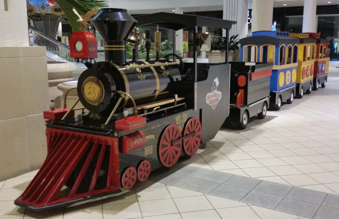 The black and red First Class Electric train with bright passenger cars inside a shopping mall
